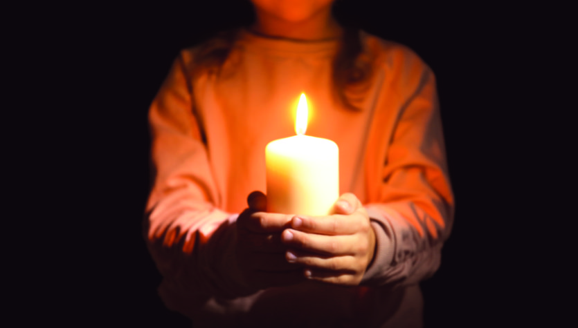 Little girl holding burning candle in darkness