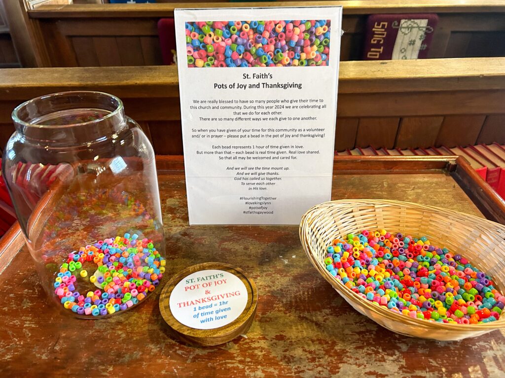 A large jar with some colourful plastic beads. Next to it is a wicker basket full of colourful beads for people to add to the pot.