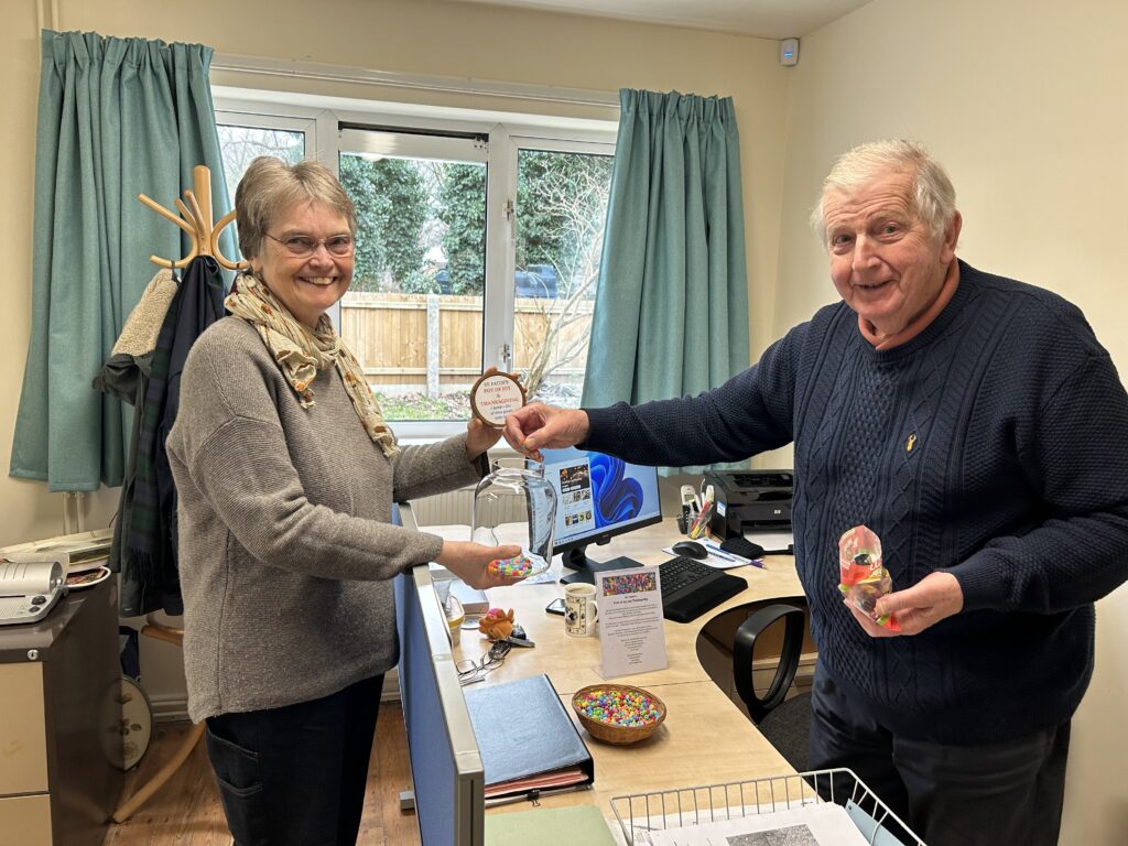 Gill and Stephen from St Faith’s Gaywood LEP Church Office. Gill is holding a glass jar and Stephen is putting a bead into the jar.