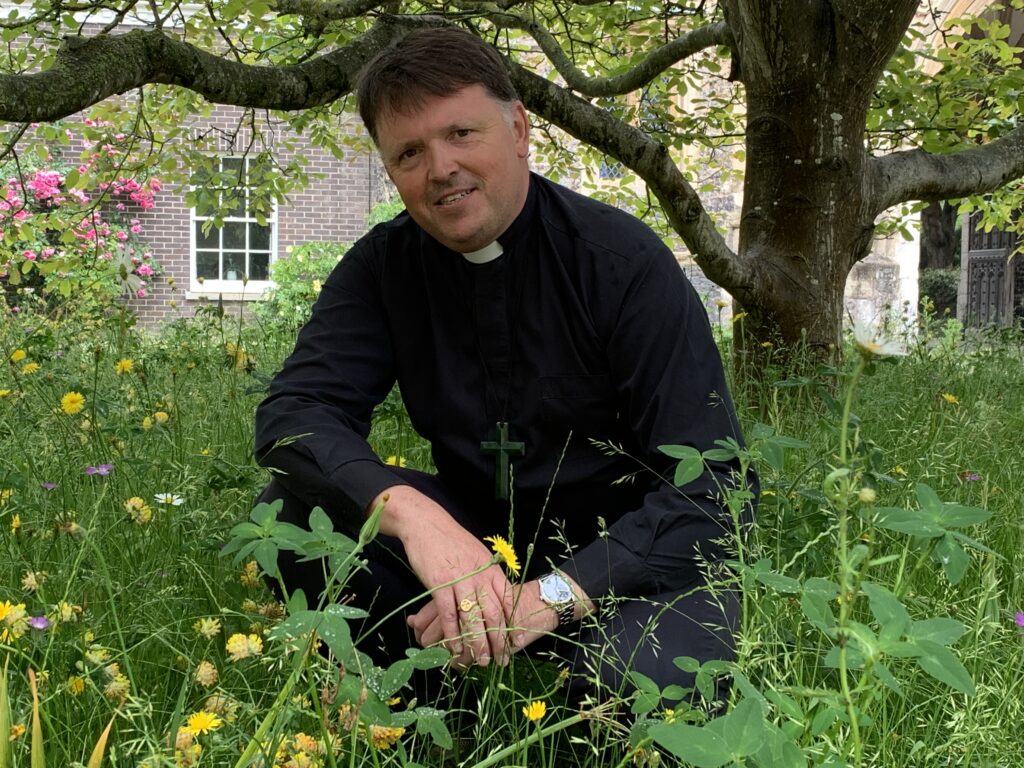 Bishop Graham in the Bishop's Garden surrounded by wildflowers