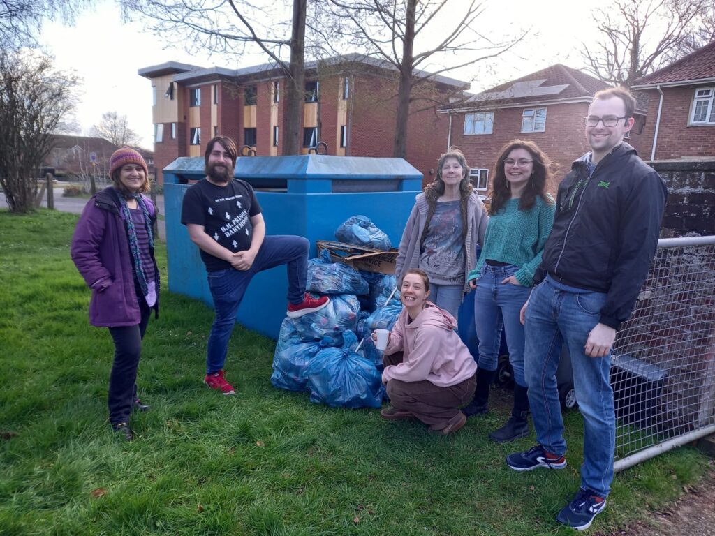 A group of people from Crossroads Earlham Church standing next to a large blue rubbish bin with lots of bags of rubbish. 